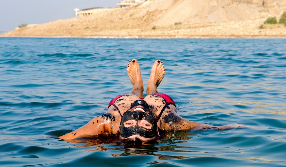 woman floating on her back in the Dead Sea after coating herself in mineral-rich mud