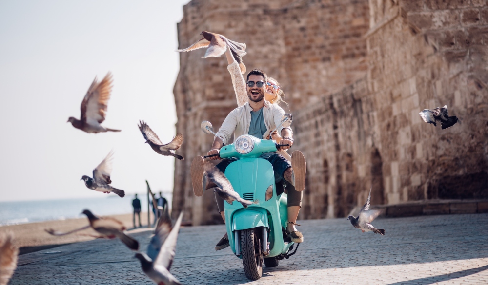 Young couple having fun riding scooter in old European town