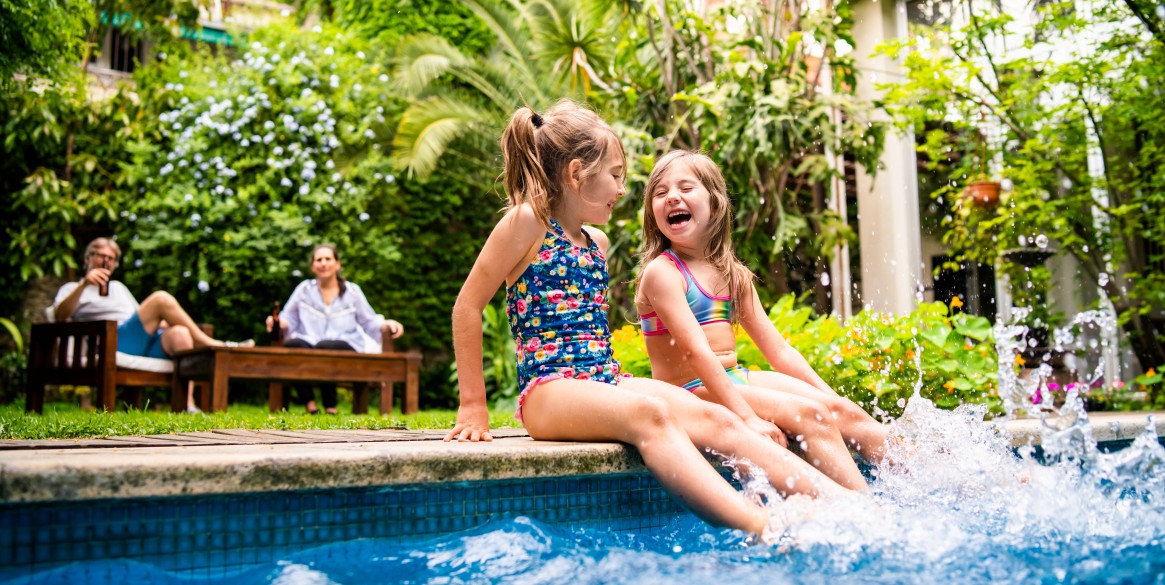Two little girls sitting at poolside and splashing water with legs