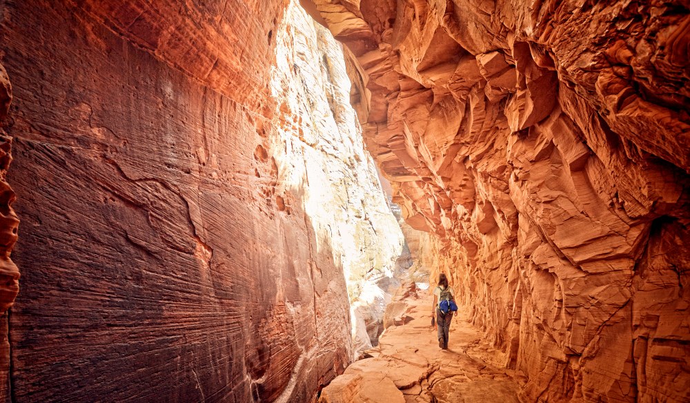 female hiker walking through red cave, best hikes in the US