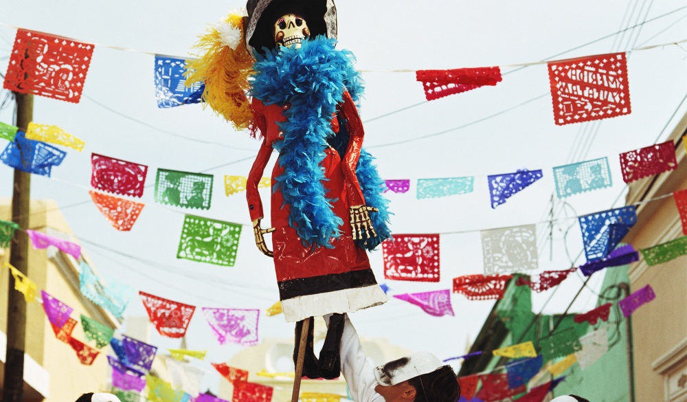 Three men wearing skeleton masks looking up at Day of the Dead puppet