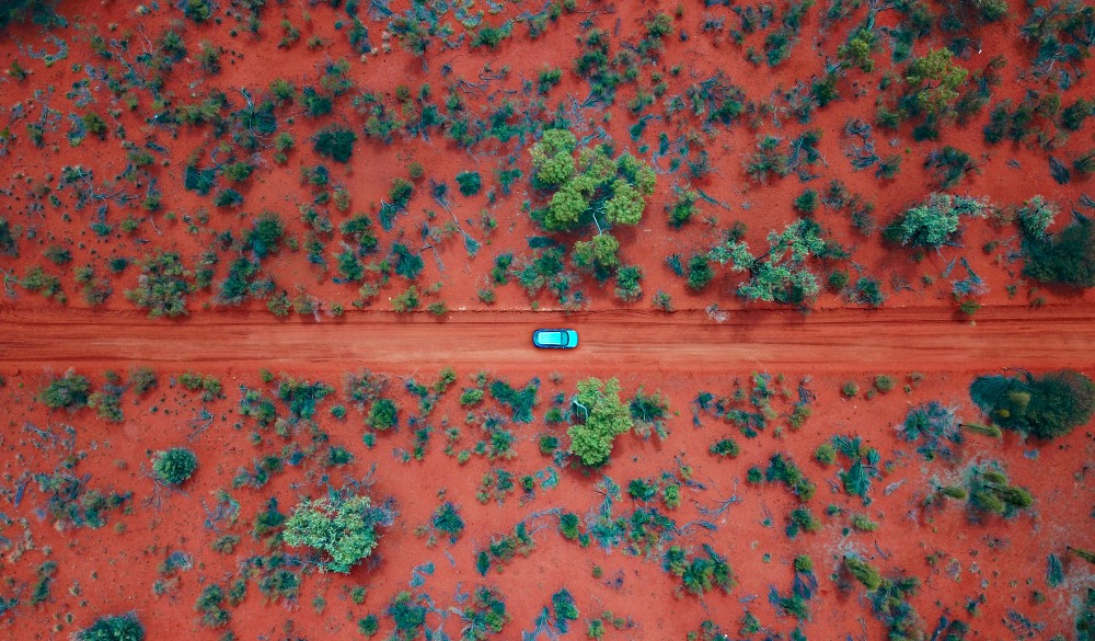 An Aerial shot of a car driving on the red centre roads in the Australian Outback