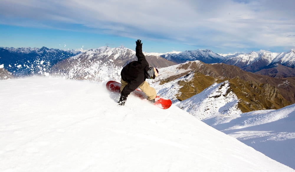 A male snowboarder blasts a heel side turn while snowboarding at Coronet Peak in Queenstown, New Zealand.