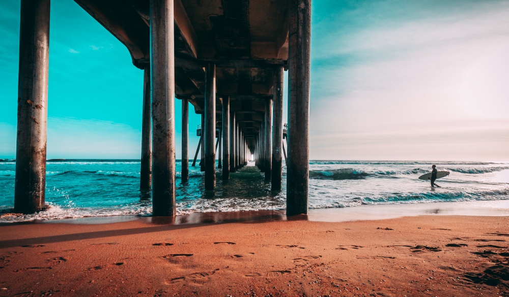 man walking next to a pier holding a surfboard