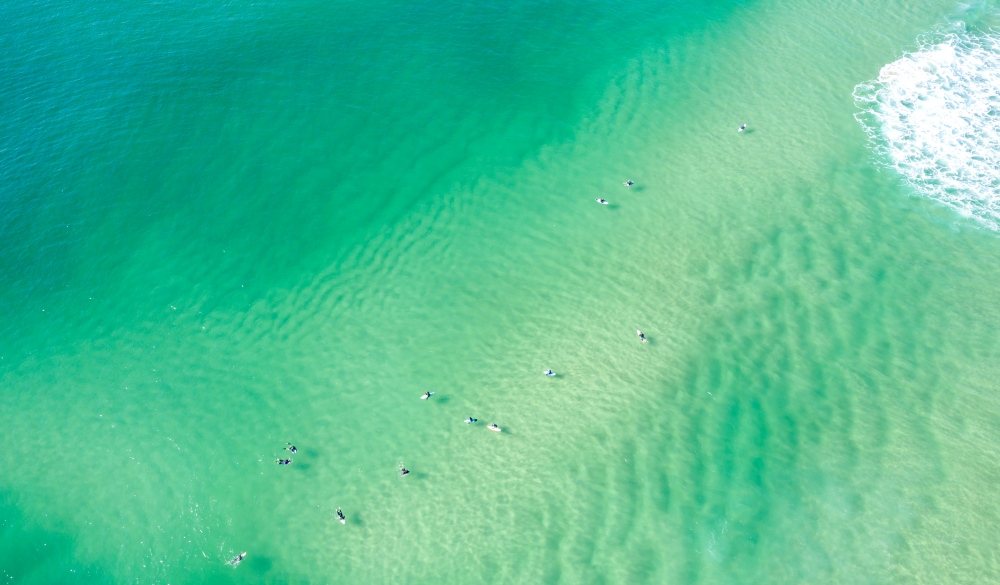 Aerial View of green and sandy ocean waters with surfers