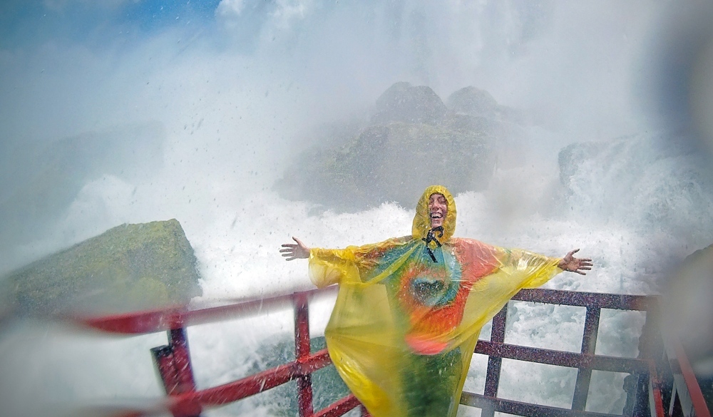 Cheerful Woman Wearing Raincoat With Arms Outstretched While Standing By Niagara Falls