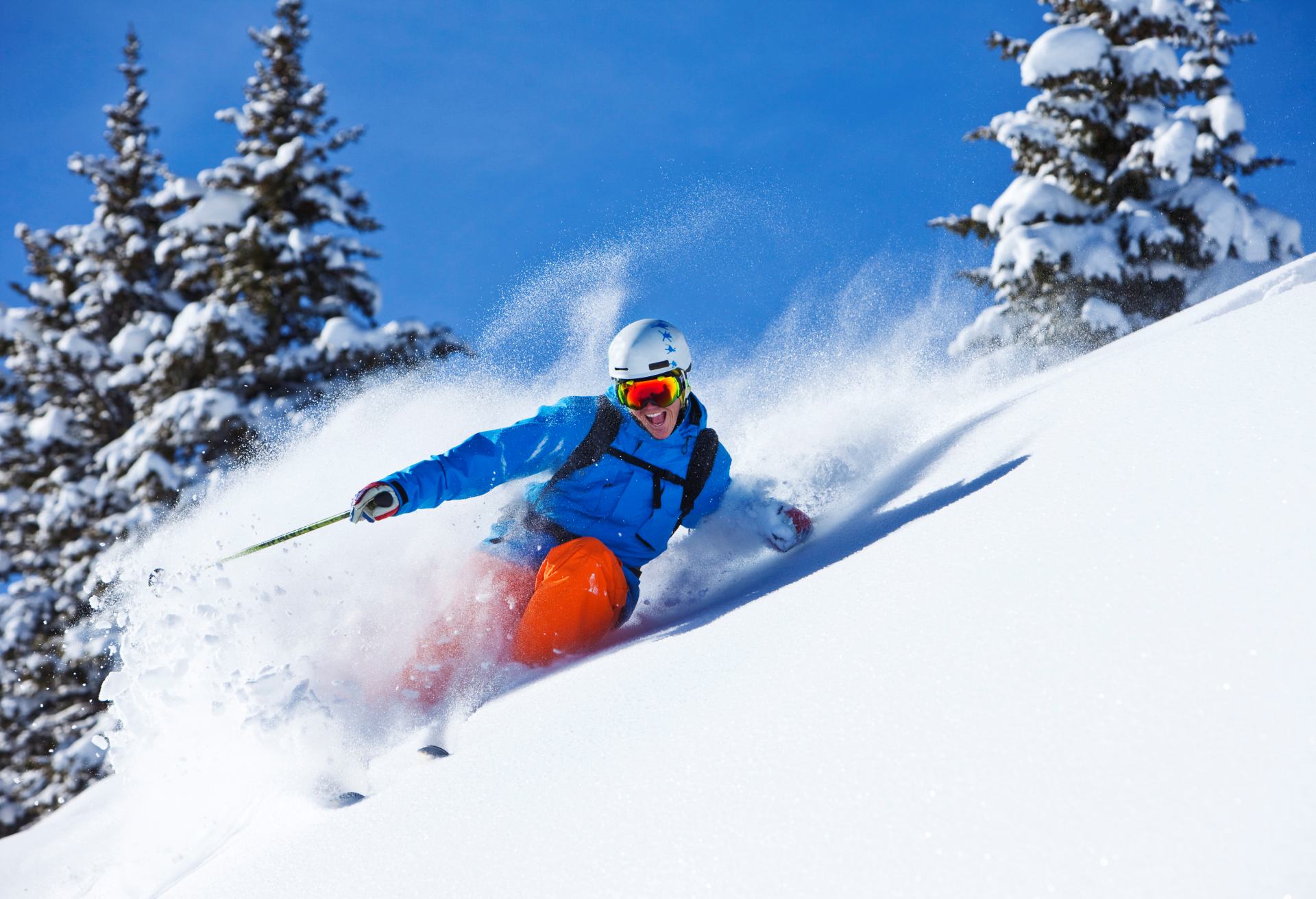 A athletic skier smiling rips fresh powder turns in the backcountry on a sunny day in Colorado.