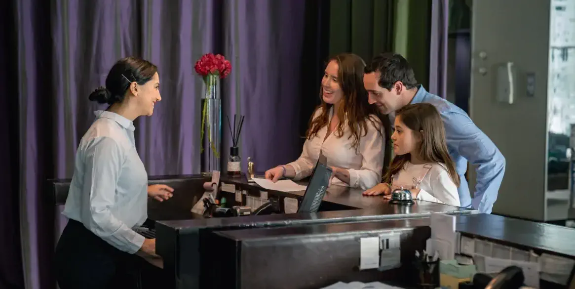 Happy couple with their daughter checking in at a luxury hotel and friendly receptionist helping them