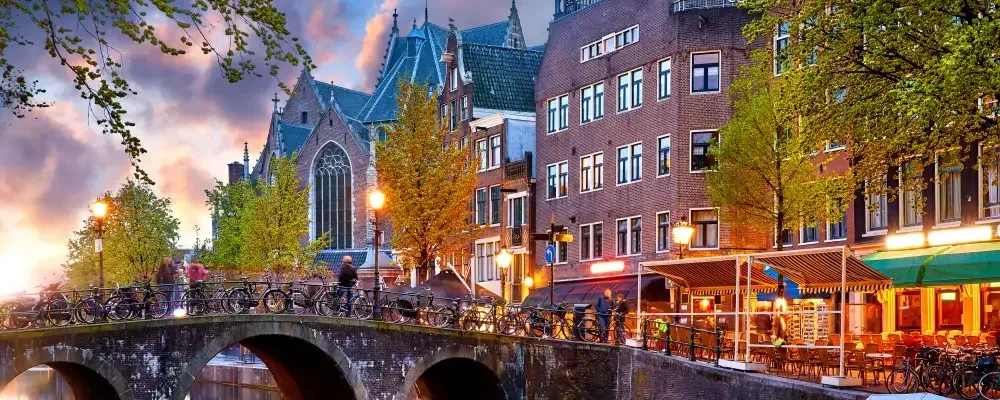 Red-light district in Amsterdam city picturesque landscape panorama evening town with pink sunset sky. Bridge over canal river Amstel.