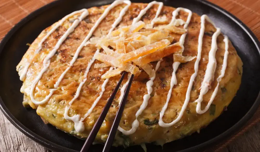 Japanese fast food: okonomiyaki on a plate close-up and chopsticks. horizontal
