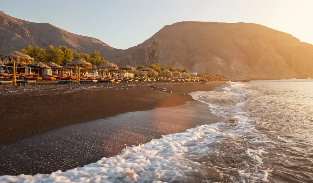 Perissa beach during sunrise on the Greek island of Santorini with sunbeds and umbrellas.