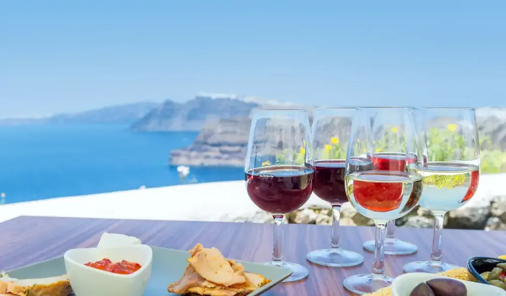 Horizontal color close-up image of greek appetizer. Tasting red, white and rose wine. Sea view in the background.