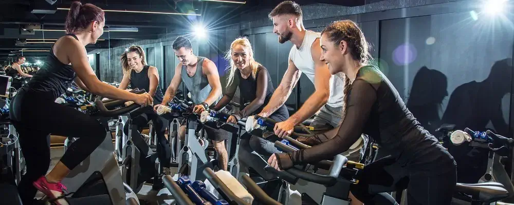 Group of attractive women and men pedaling on a stationary bikes at the gym.
