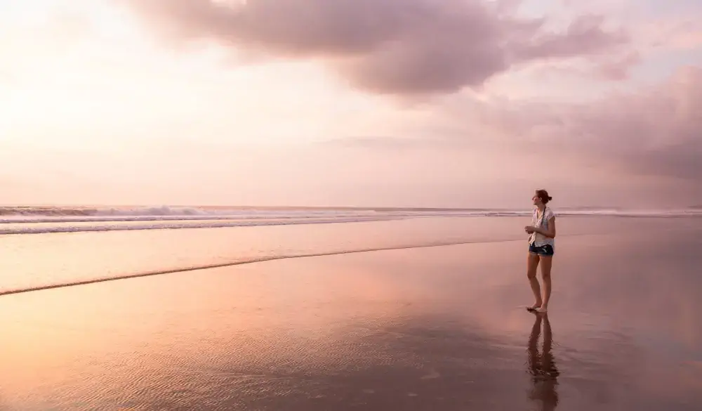 The Beach between Legian and Seminyak just before sunset. One attractive young woman is walking on the sandy beach in the shallow waters. Seminyak beach, Kuta, Bali, Indonesia.