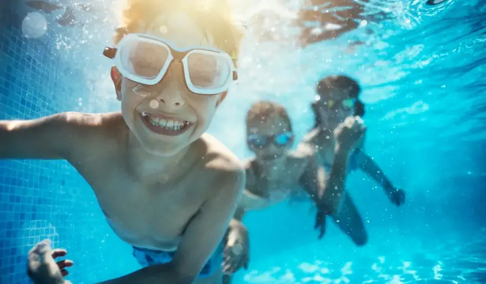 Happy kids having underwater party in the swimming pool. The boy is grinning at the camera.
Shot with Nikon D850.