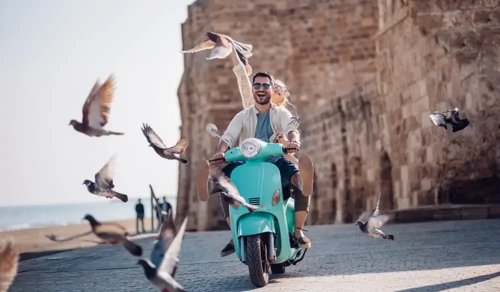 Young couple having fun riding scooter in old European town