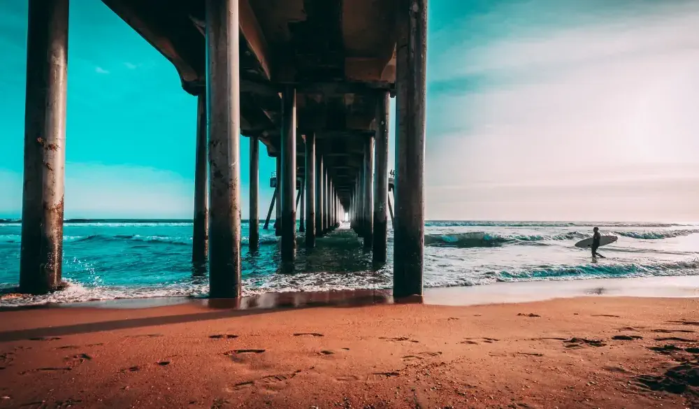 man walking next to a pier holding a surfboard