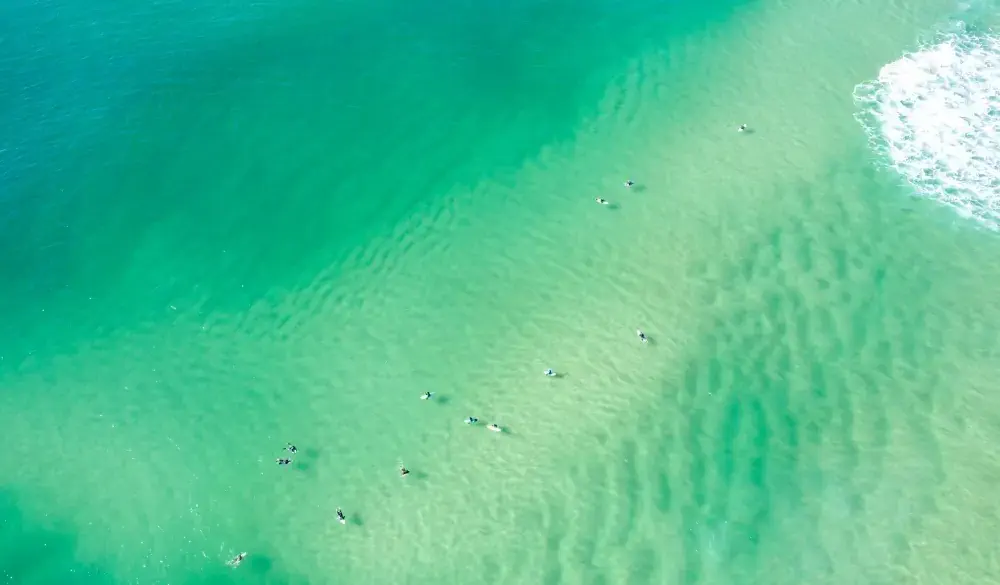 Aerial View of green and sandy ocean waters with surfers