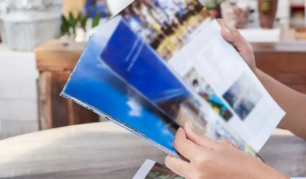 Cropped Hand Of Person Holding Magazine On Table